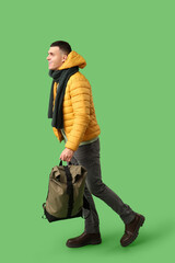 Young man in yellow stylish puffer jacket and scarf with bag on green background