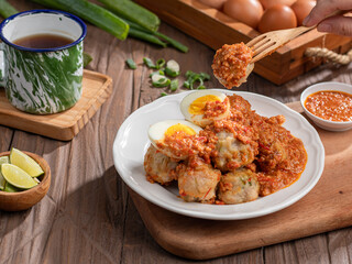 A plate of traditional siomai, a type of Indonesian steamed dumpling served with a spicy peanut sauce and accompanied by hard-boiled eggs. a hand holding a fork is lifting a piece
