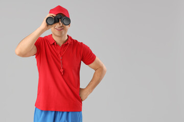 Happy male lifeguard with binoculars on grey background