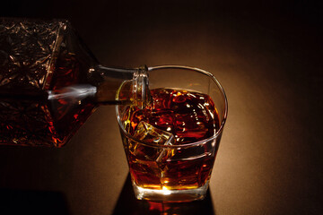 Whiskey being poured into a glass with ice on a dark background