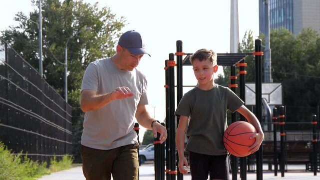 A father teaches his son how to play basketball. a happy boy walks with a basketball with his dad on the sports ground. the concept of family sports.