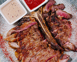 Sliced grilled t-bone steak lying on plate with sauces