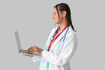 Young African-American female doctor with stethoscope and laptop on white background