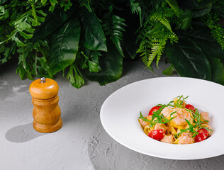 Tagliatelle with shrimps and tomatoes served on white plate near pepper mill