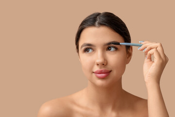 Young woman correcting shape of her eyebrows on brown background