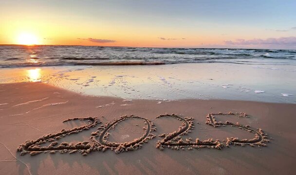 handwritten text of 2025 on a sandy surface at the beach, concept of the New Year, Welcoming the year 2025. Happy New Year. Seashore, waves, sand.