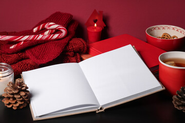 Beautiful winter composition with book, cup of tea, Christmas snacks and warm sweater on red background