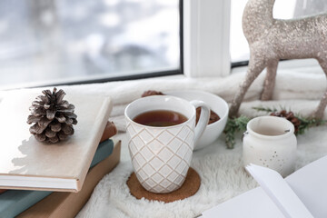 Beautiful composition with books, cup of tea, Christmas decorations and sweet snacks on windowsill