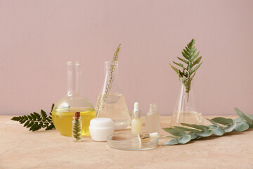 Laboratory glassware with ingredients and samples for preparing natural cosmetics on beige table near pink wall
