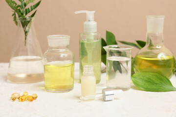 Laboratory glassware with ingredients and samples for preparing natural cosmetics on white table near beige wall