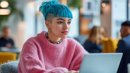 Young woman with blue hair in pink sweater using laptop in modern cafe, focused and creative, working on her project.