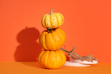 Decorative podiums with autumn leaf and fresh pumpkins on orange background