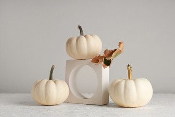Decorative podium with fresh pumpkins and autumn leaf on grey background