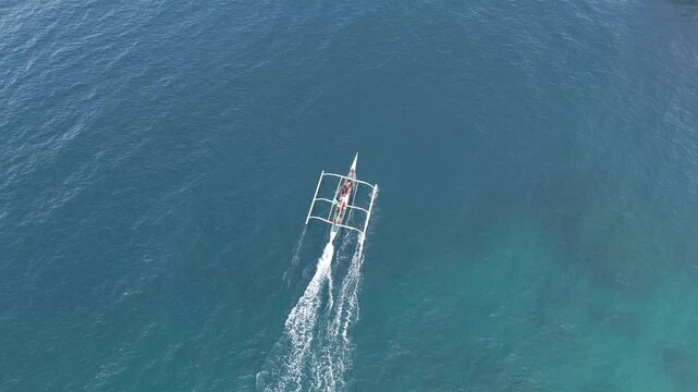 A traditional filipino banka boat cruising over clear blue ocean waters in the philippines, aerial view