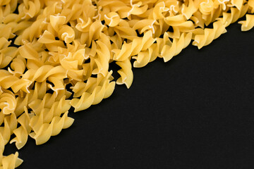 Uncooked Fusilli Pasta with Copy Space on Black Background. Raw and Dry Macaroni. Fat and Unhealthy...