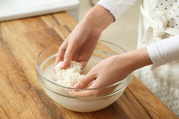 Woman rinsing rice in glass bowl near wooden table, closeup