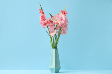 Vase with bouquet of beautiful gladiolus flowers on blue background