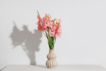Vase with bouquet of beautiful gladiolus flowers on table against white background
