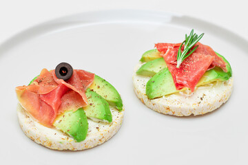 Rice Cake Sandwich with Avocado, Jamon, Olives and Rosemary on White Plate. Easy Breakfast. Quick and Healthy Sandwiches. Crispbread with Tasty Filling. Healthy Dietary Snack - Isolation