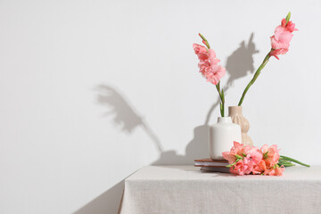 Vases with beautiful gladiolus flowers and books on table against white background