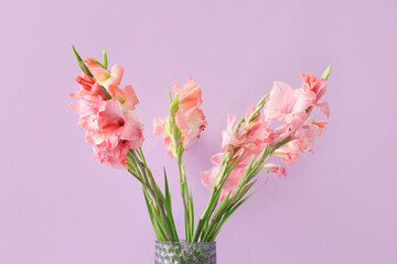 Glass vase with bouquet of beautiful gladiolus flowers on lilac background