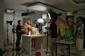 Cameraman shooting model in domestic studio while his colleagues preparing her for process