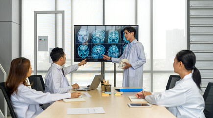 Young medical professional standing and presenting, holding a model of human skull and referencing...