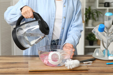 Woman pouring water into bowl with baby bottles in kitchen, closeup