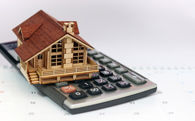 A calculator and a wooden house are placed on the calendar. Business investment and real estate concepts.
