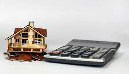 On a white background lies a calculator and a slanted house on top of a pile of coins. instability...