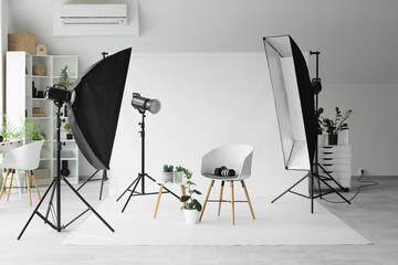 Chair with houseplants, photo camera and lighting equipment in modern studio