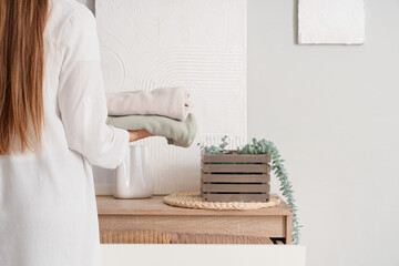 Young woman putting stack of clean clothes into dresser at home