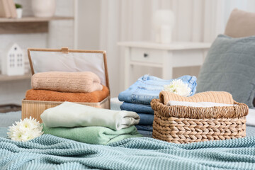 Wicker baskets with stacks of stylish clothes and flowers on bed in room
