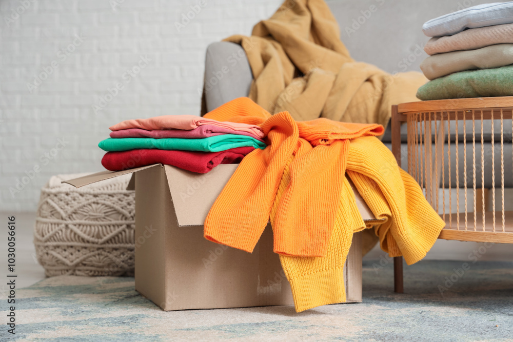 Poster Cardboard box with stacks of stylish clothes on coffee table in living room