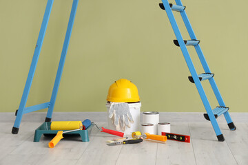 Stepladder with cans of paint and tools near green wall