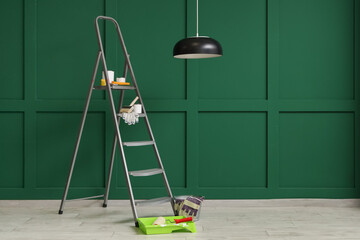 Stepladder with cans of paint and tools near green wall