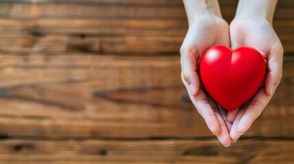 Closeup of hands holding a red heart on a wooden background.