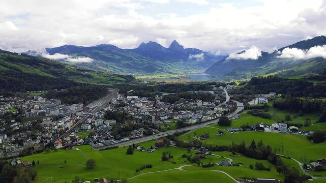 Panoramic cinematic view of a peaceful Swiss city in a green valley surrounded by rolling hills and rocky peaks and the serene Lake Lauerz with the iconic Grosser Mythen mountains in Switzerland 