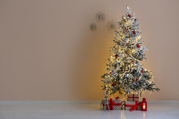 Decorated Christmas tree with glowing lights and gift boxes near beige wall