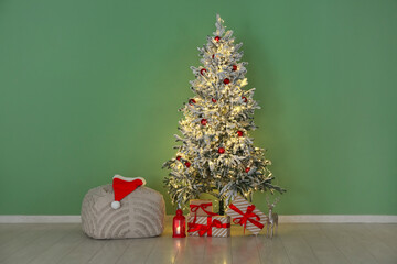 Decorated Christmas tree with glowing lights and gift boxes near green wall