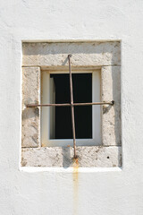 A close-up of a wall featuring a small, barred window framed in stone