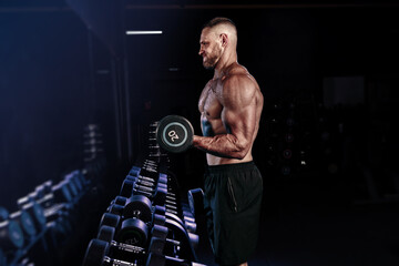 Muscular man training with weights. Brutal strong athletic men pumping up muscles workout in dark gym.