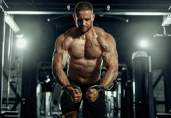 Muscular man training with weights. Brutal strong athletic men pumping up muscles workout in dark gym.
