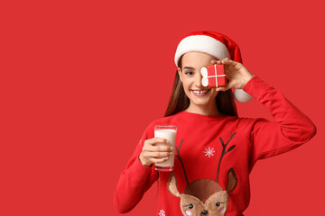 Young woman with tasty Christmas gingerbread cookie and glass of milk on red background