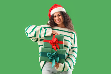 Pretty young African-American woman with Christmas gift boxes on green background