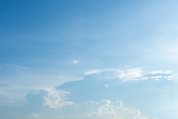Fluffy white clouds drift beneath a clear blue sky as a lone airplane soars high above, casting a long shadow on the vast expanse