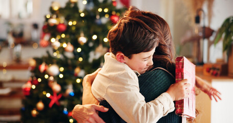 Christmas, gift and hug with mother, son and bonding together with decoration, house and festive in lounge. Xmas tree, family and parent with boy, embrace and present with happiness, holiday and love