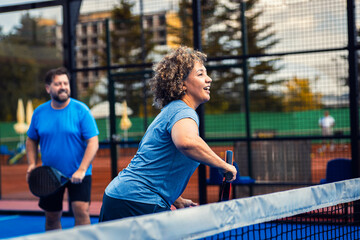 Mixed adult couple palying padel on outdoor court.