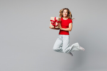 Full body young smiling happy woman she wears red t-shirt casual clothes jump high hold in hand present box with gift ribbon bow isolated on plain grey background studio portrait. Lifestyle concept.