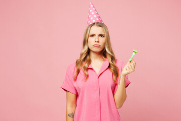 Young sad dissatisfied upset displeased woman wear shirt cone hat celebrating birthday holiday hold in hand blowing pipe look camera isolated on plain pastel light pink background. Lifestyle concept.